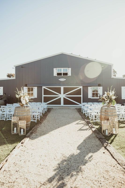 The barn's front doors set for a wedding ceremony with white chairs, wine barrels and florals.