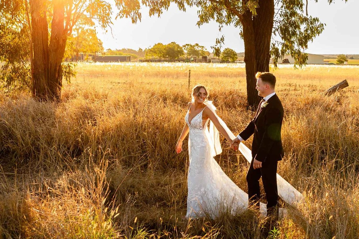 A couple hand in hand in Aberfeldy Barn's golden long-grass paddock at sunset.