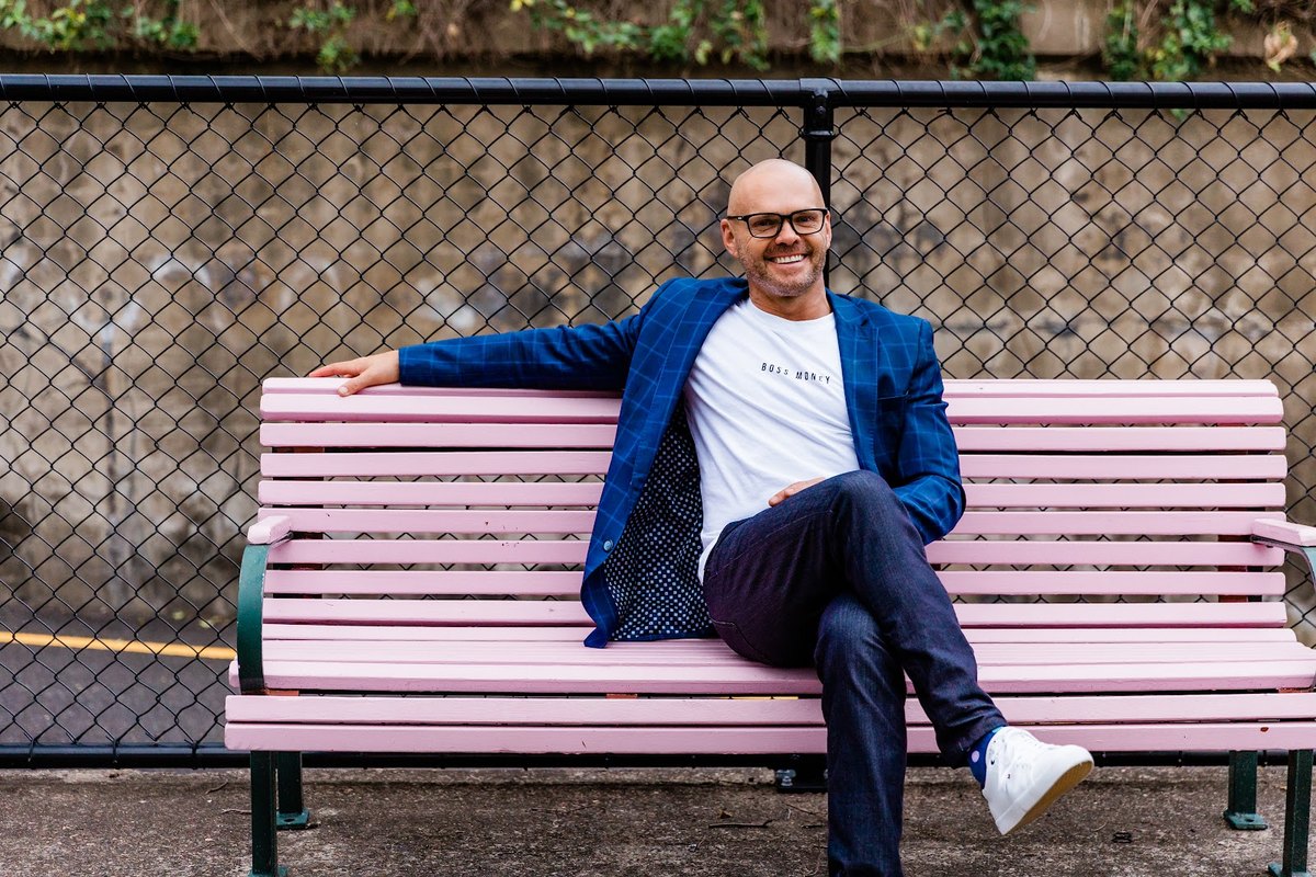 Boss Money founder Tom Uhlich sitting on a pink bench in a blue blazer.
