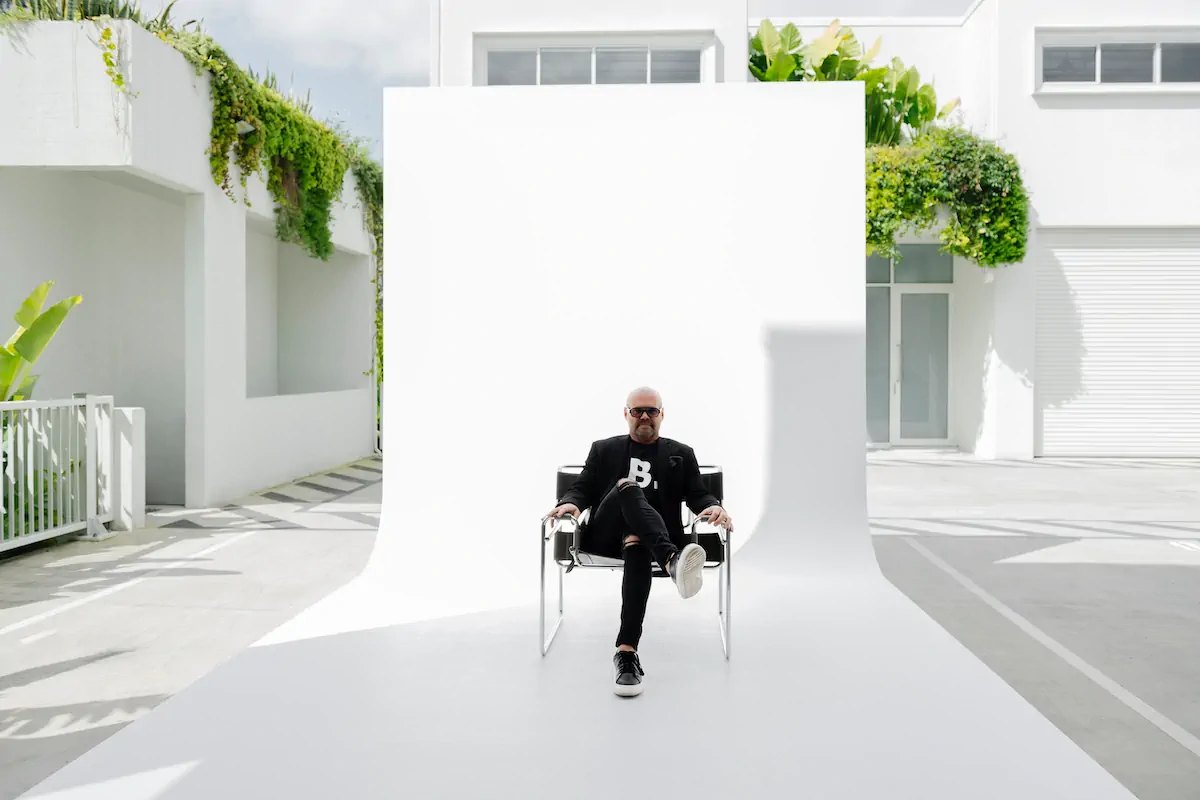Tom Uhlich seated on a chair in front of a white photography backdrop.