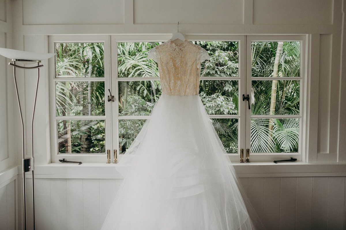 A wedding dress hanging in the white casement windows of Bower Cottage against the rainforest.