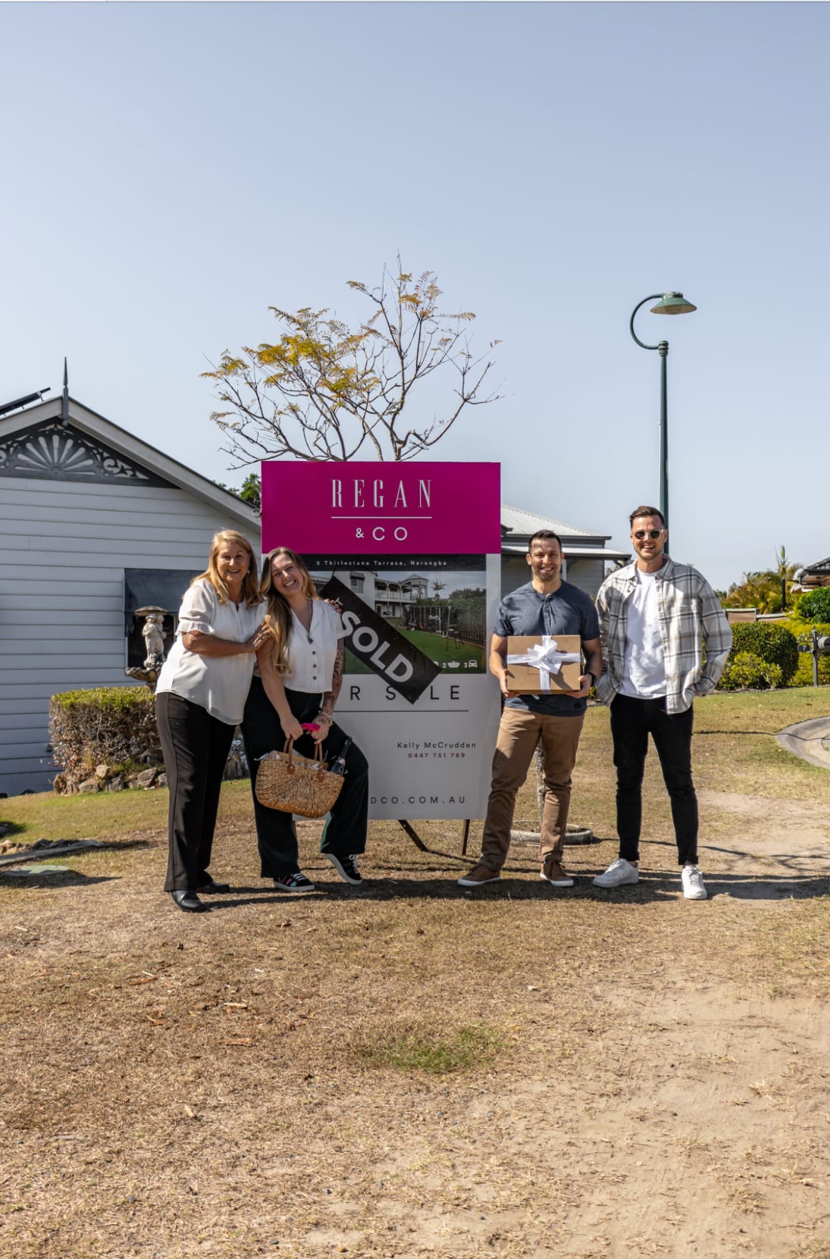 Four adults standing beside a property sign marked sold.