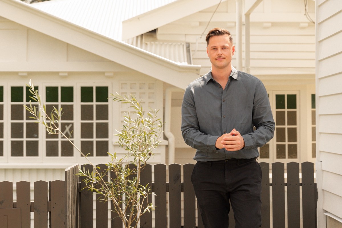 Jack Freestone of Buyers Collective outside a white weatherboard home, beside a timber gate.