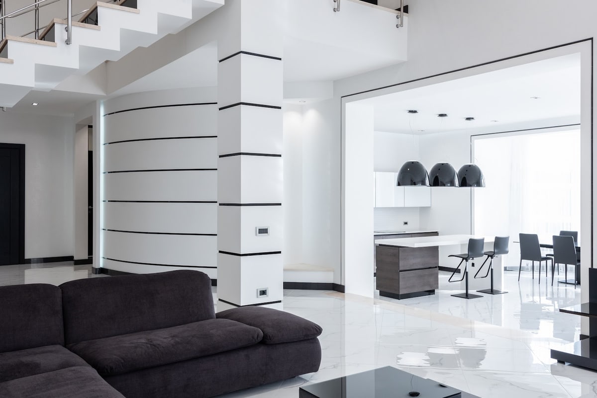A bright modern living room with a dark sofa and an open kitchen and dining area.