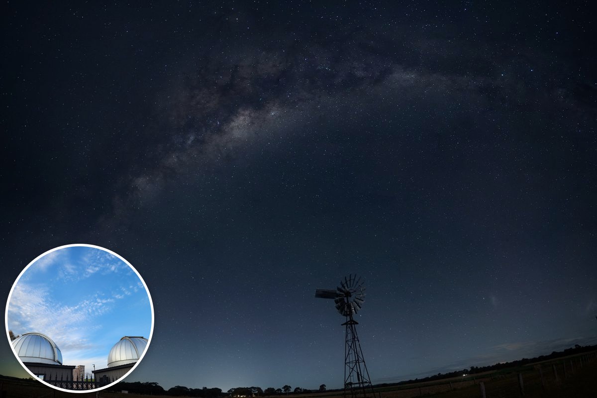 The Milky Way arcs over a rural windmill in a dark night sky.